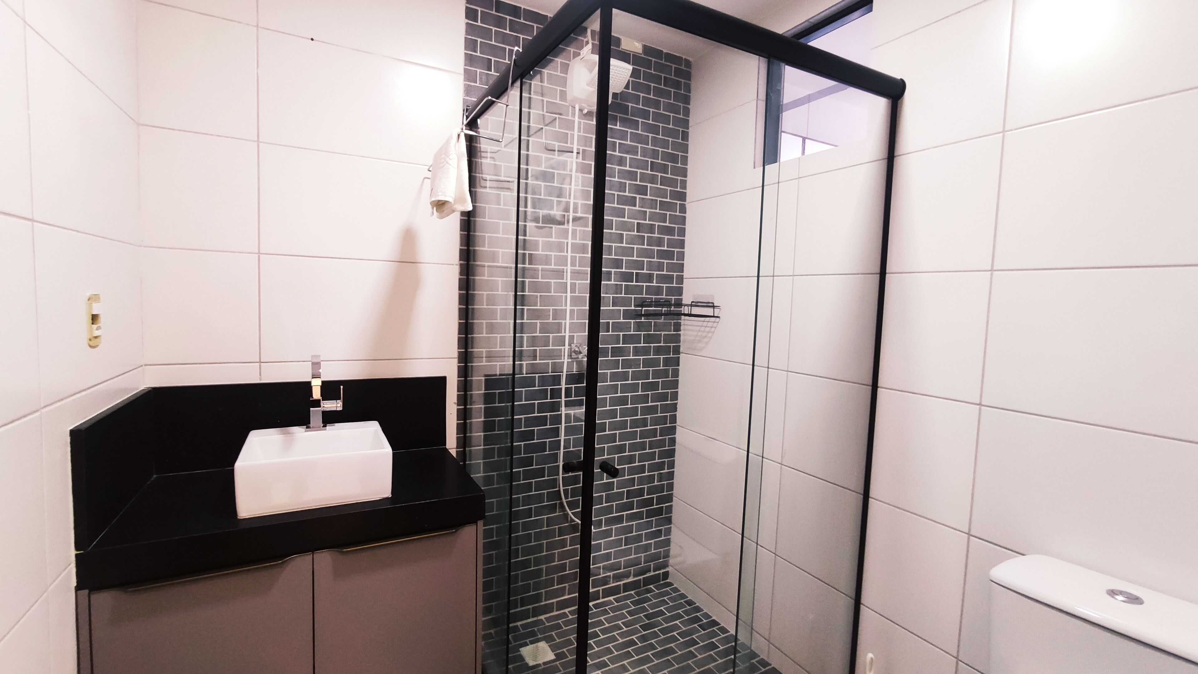 A modern bathroom with a glass shower enclosure, a black countertop with a sink, and a white towel hanging on the wall.