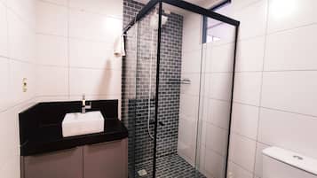 A modern bathroom with a glass shower enclosure, a black countertop with a sink, and a white towel hanging on the wall.
