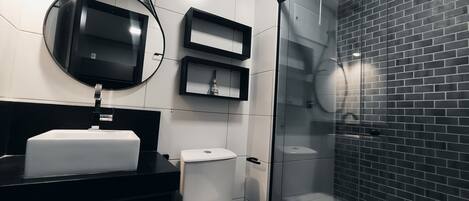 Une salle de bain moderne avec un plan de toilette noir, des toilettes, une douche en verre et un miroir.
