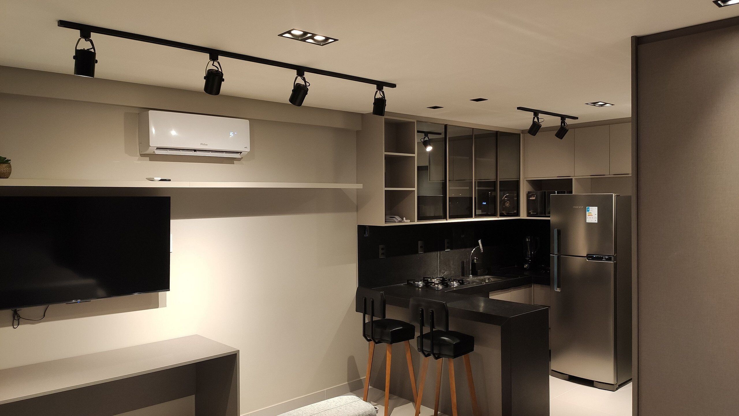 A modern kitchen with a built-in refrigerator, a flat-screen TV, and a coffee machine.