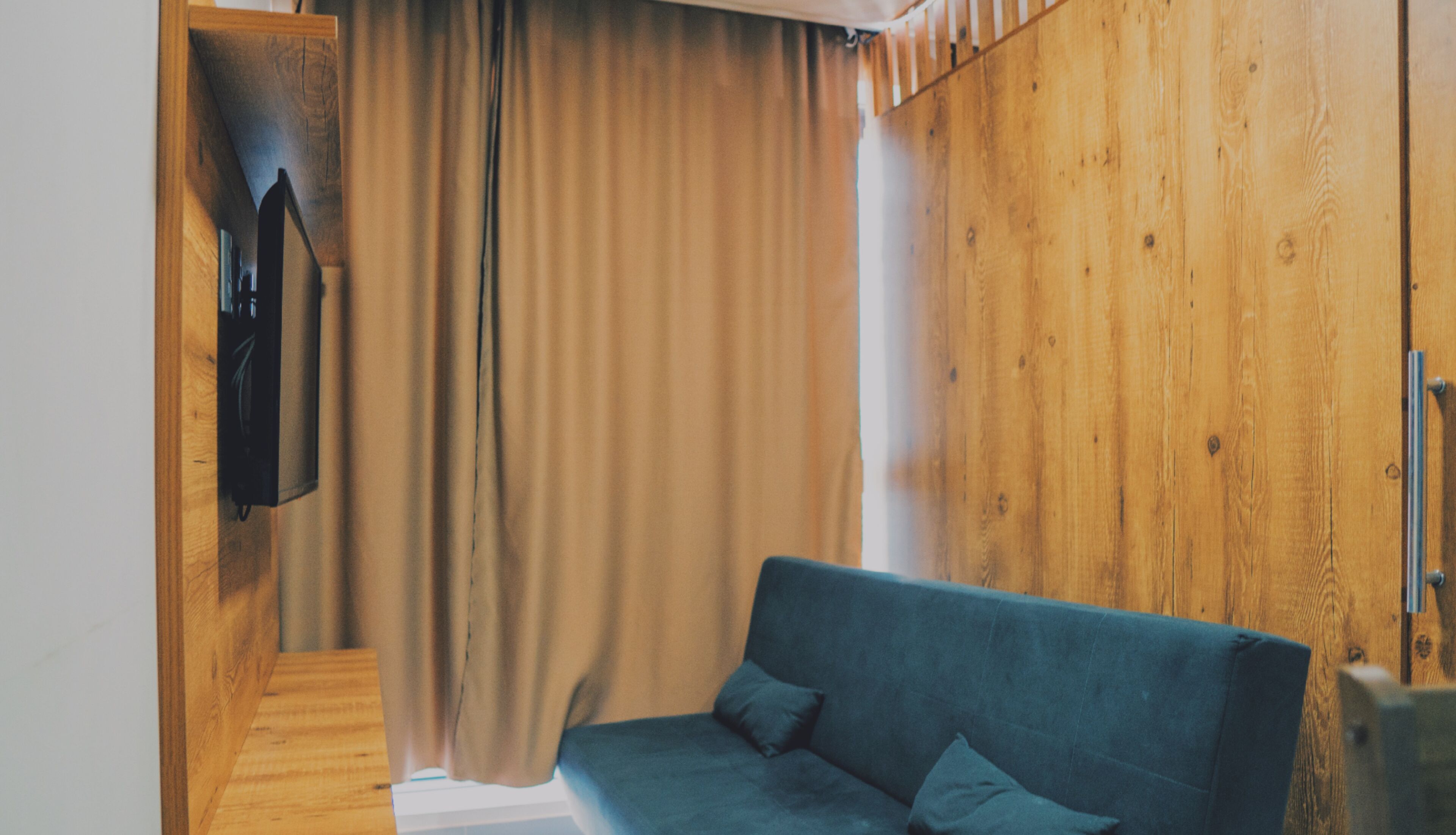 Una habitación con pared de madera, sofá azul y una cortina.