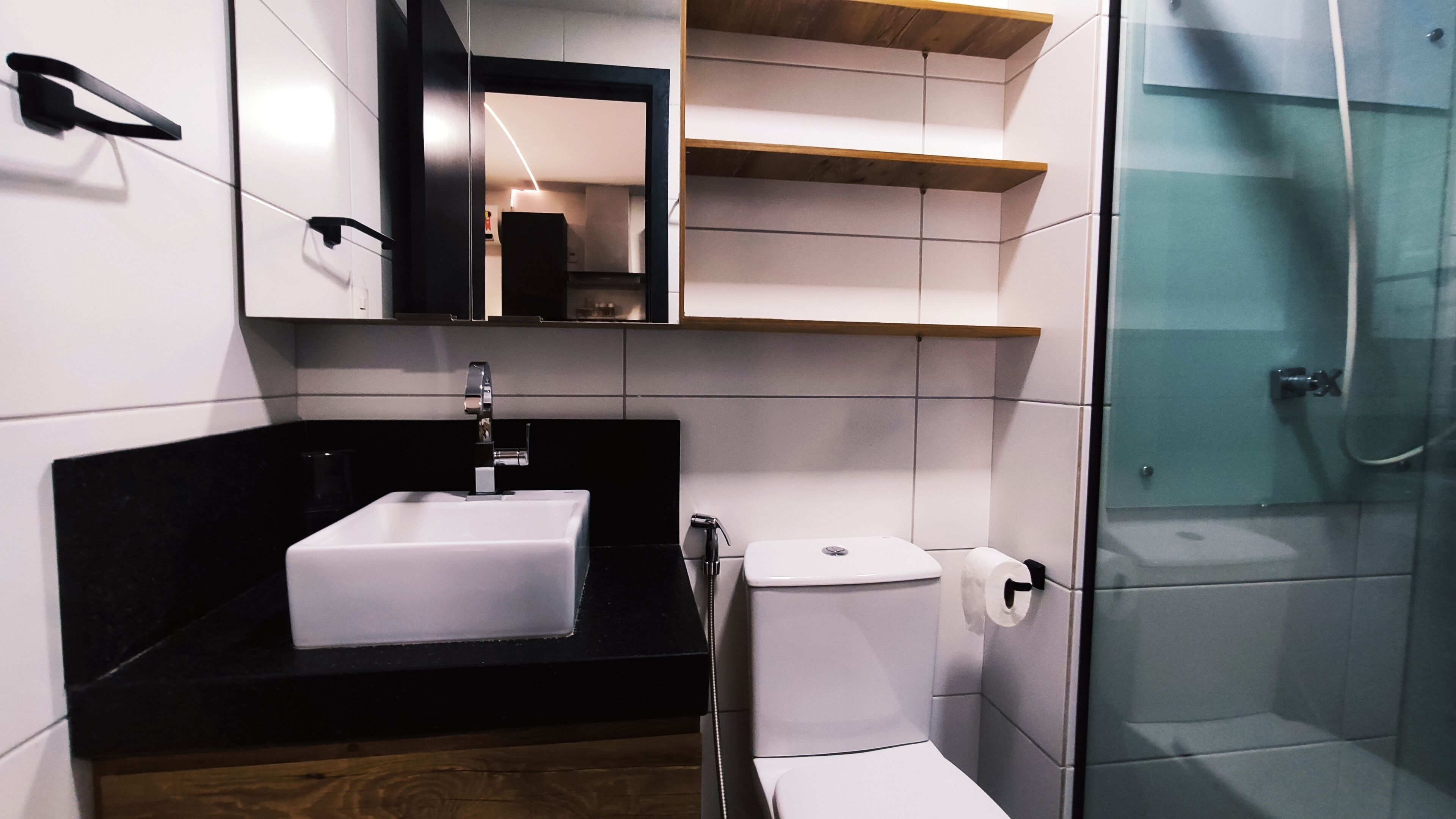 Une salle de bain moderne avec un lavabo blanc, un plan de toilette noir et une douche à parois de verre.