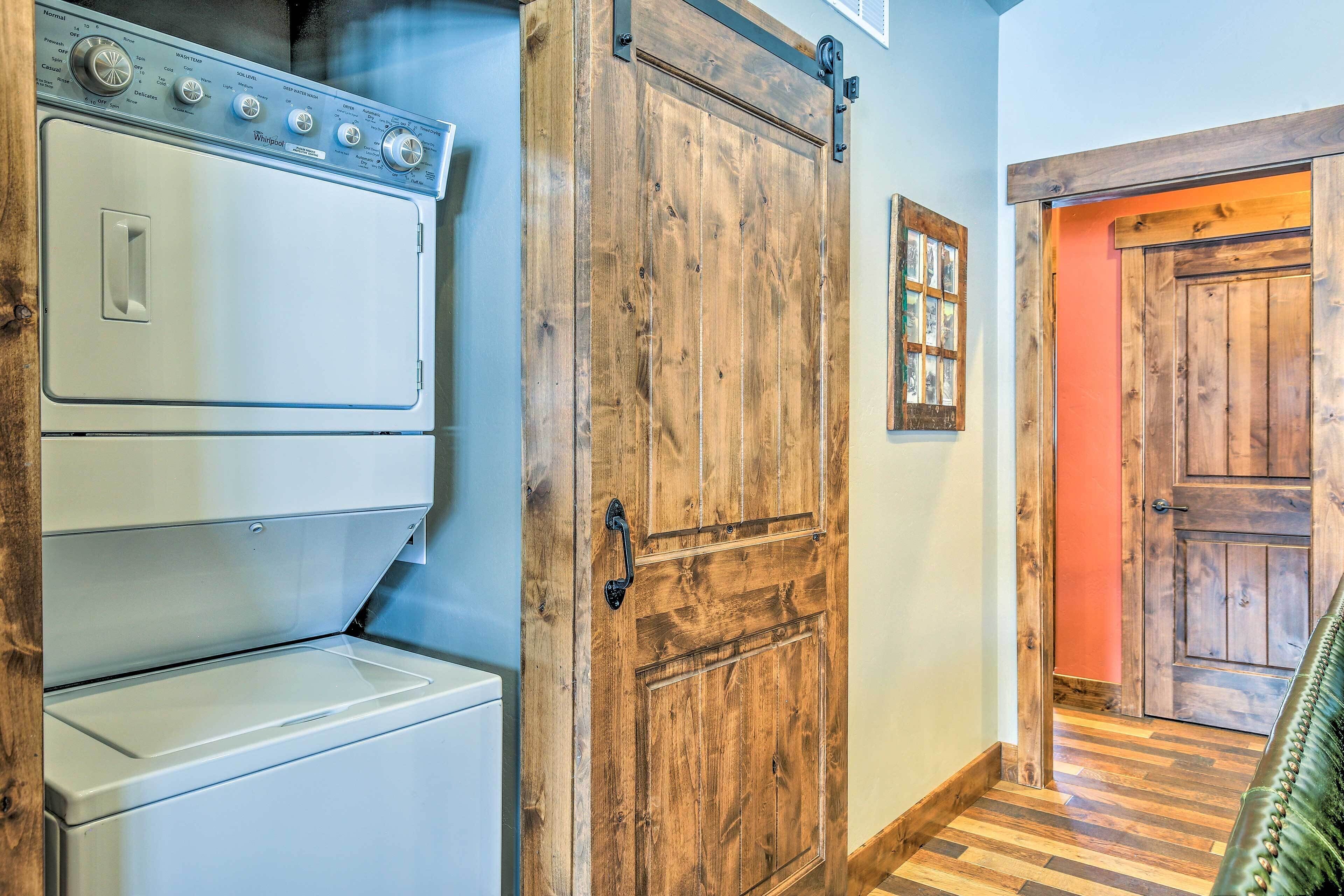 Un cuarto de lavado con lavadoras y secadoras apiladas, una puerta de madera y un pasillo que conduce a otra habitación.