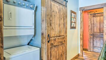 Un cuarto de lavado con lavadoras y secadoras apiladas, una puerta de madera y un pasillo que conduce a otra habitación.