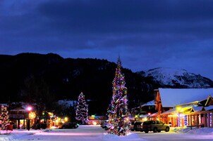 A snowy town square with Christmas trees and illuminated buildings.