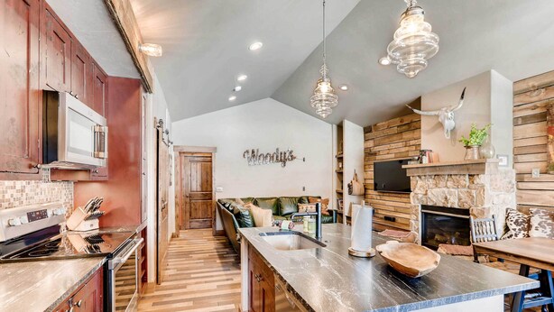 A modern kitchen with wooden cabinets, a large island, and a stone fireplace. - 2 Blocks To Grand Lake: Downtown Western Cabin! (Grand Lake)