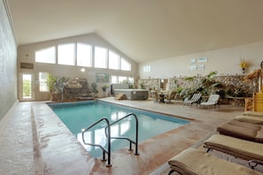 Une piscine intérieure avec un mur en pierre, des chaises longues et une cheminée en pierre.
