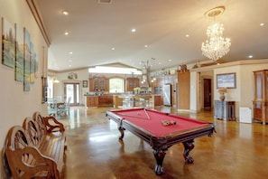 Un vaste espace de vie comprenant une table de billard, des meubles en bois et un lustre.