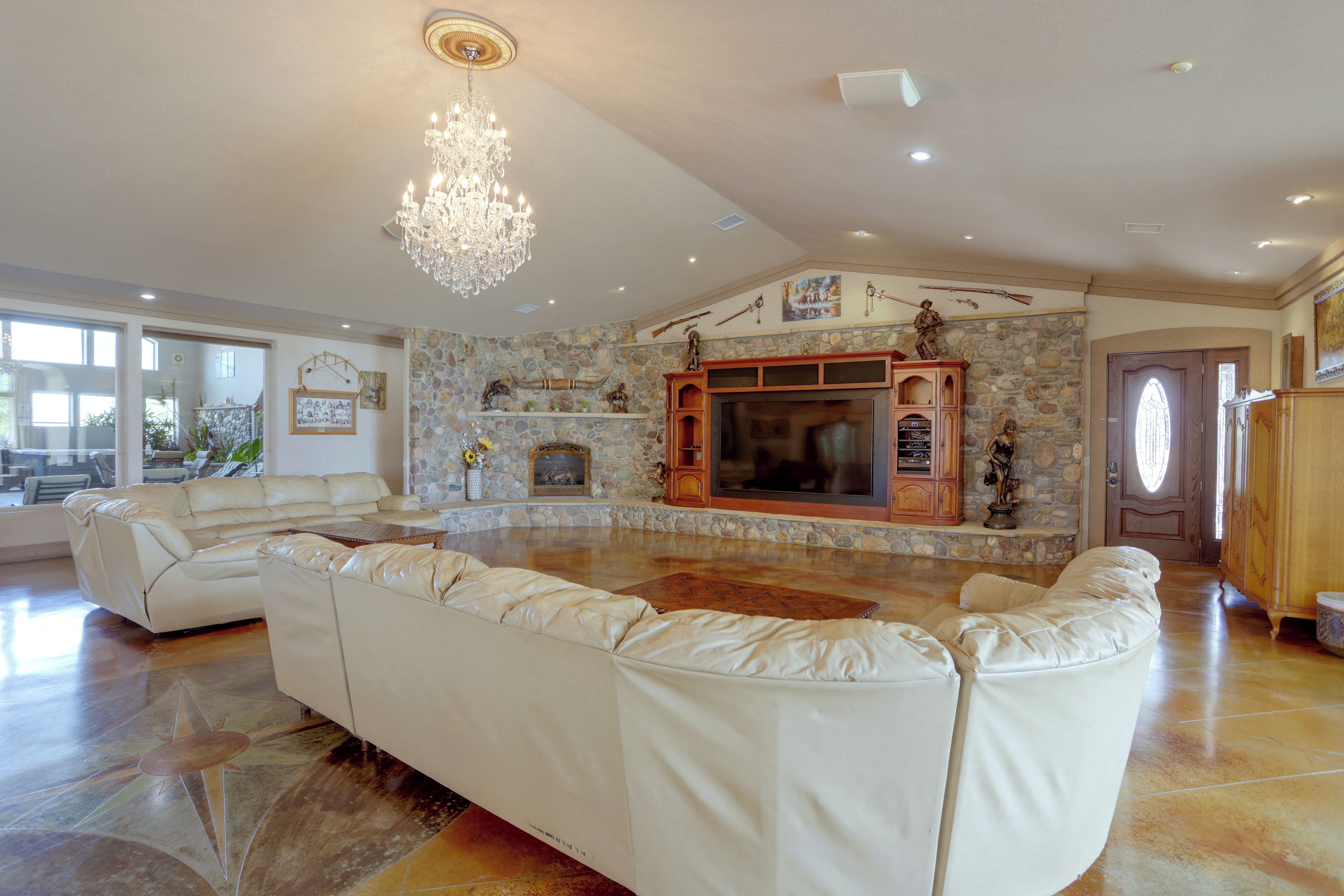 Amplia sala de estar con un sofá grande de cuero blanco, una chimenea de piedra y un candelabro.