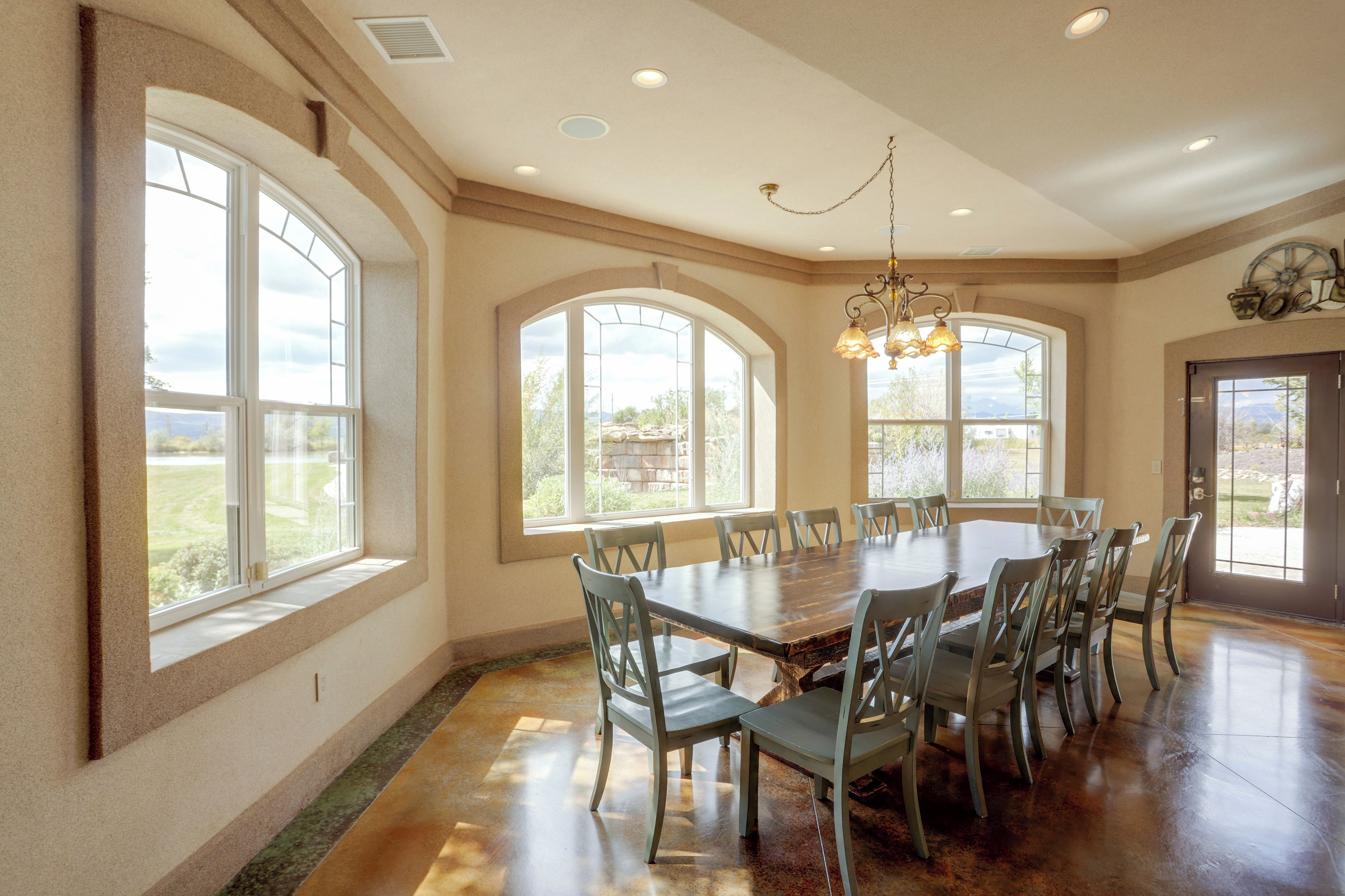 A spacious dining area with a large wooden table and multiple chairs, surrounded by large windows offering views of the outdoors.