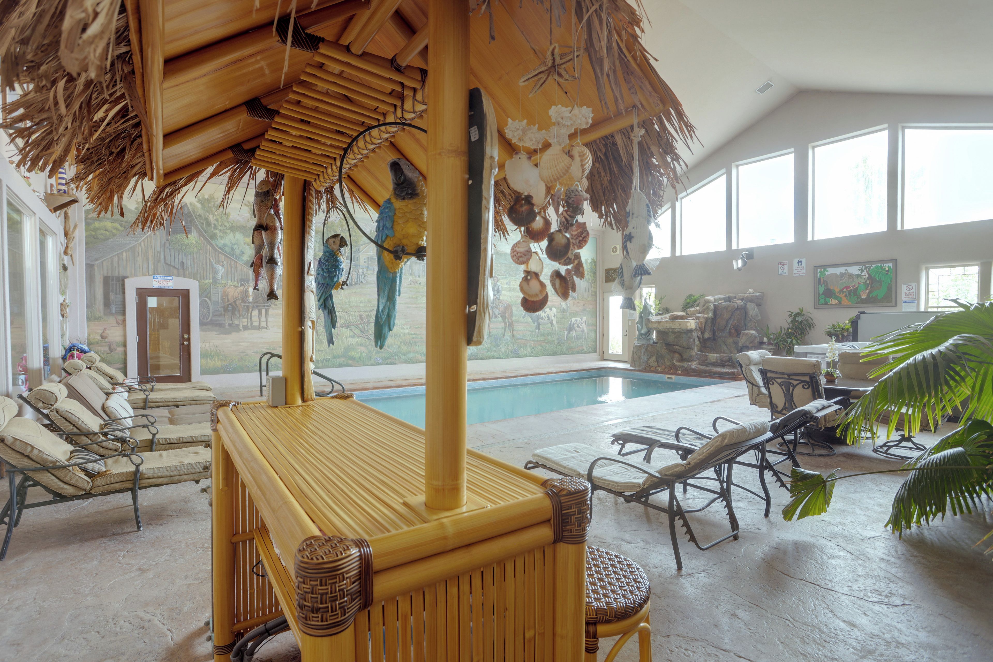 Un área junto a la piscina con sillones de descanso, una mesa de bambú y un techo de paja.