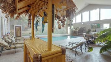 Un área junto a la piscina con sillones de descanso, una mesa de bambú y un techo de paja.