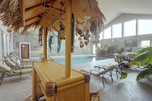 Un espace aménagé au bord de la piscine, avec des chaises longues, une table en bambou et un toit de chaume.