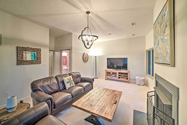 A living room with a leather sofa, a wooden coffee table, a chandelier, a television, and artwork on the walls.
