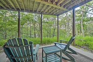 A covered outdoor seating area with Adirondack chairs and a table, surrounded by a forested landscape.