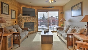 A cozy log cabin interior with a stone fireplace, wooden furniture, and a large TV mounted on the wall. - Mountainside Grand Lake Condo w/ Patio! (Grand Lake)