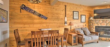 A cozy room with a wooden wall, a fireplace, a dining table with chairs, and a sofa.