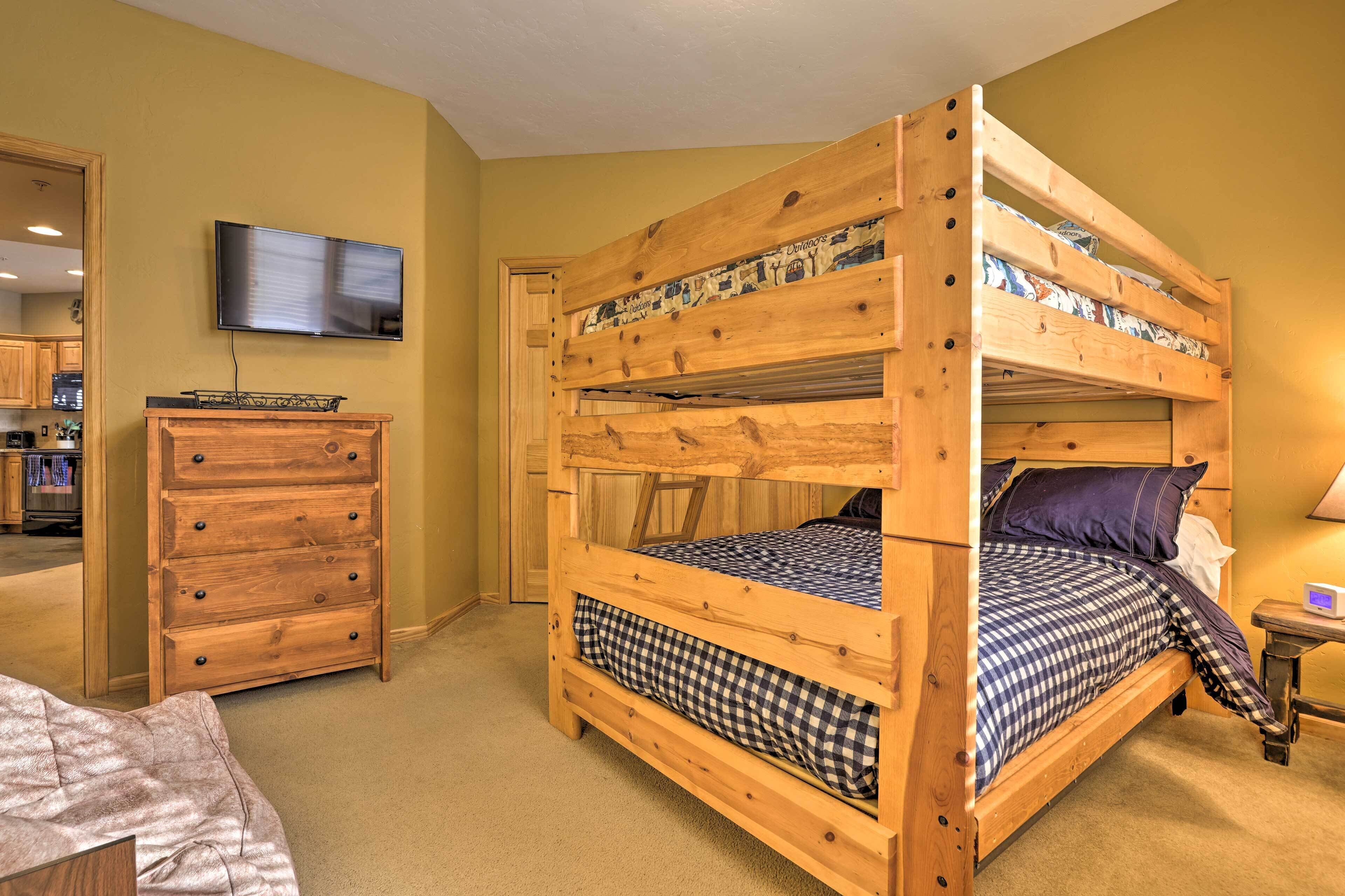 Un lit superposé avec un téléviseur fixé au mur, une commode en bois et une petite table avec une lampe.