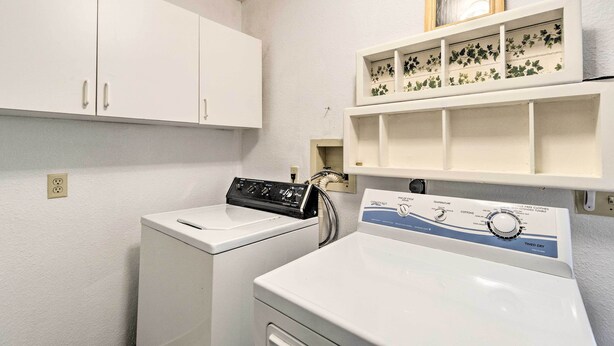 A laundry area with a front-loading washer and dryer, a shelf with decorative items, and a white cabinet. - Charming Port Charlotte Home w/ Lanai & Pool! (Port Charlotte)