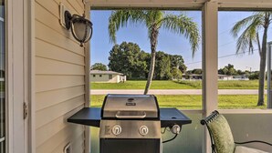A grill on a porch with a view of a residential area and palm trees. - Charming Port Charlotte Home w/ Lanai & Pool! (Port Charlotte)