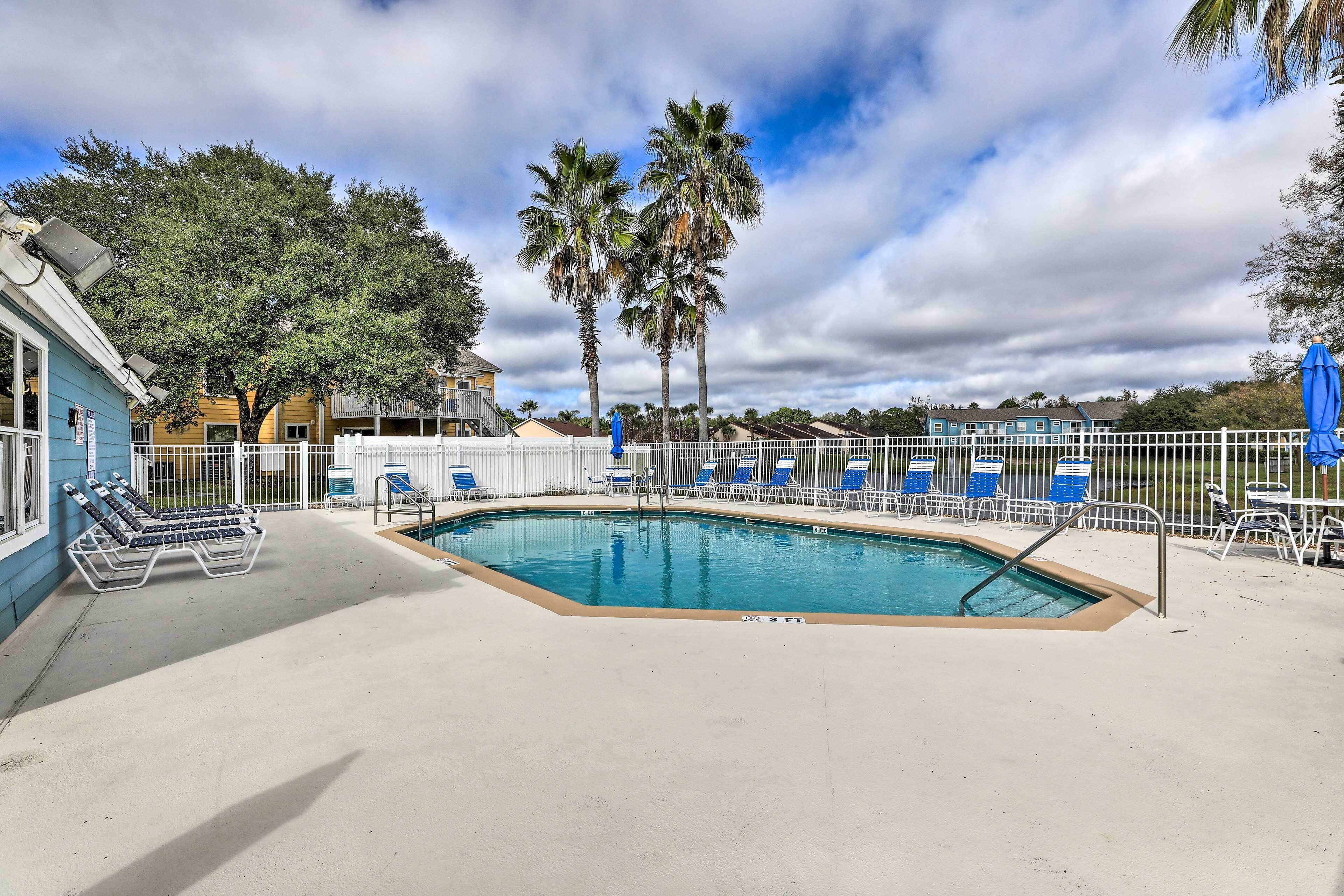 A swimming pool with blue lounge chairs and palm trees in the background.