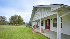 Et hvidt hus med rødlakeret hoveddør, en veranda og en græsplæne.