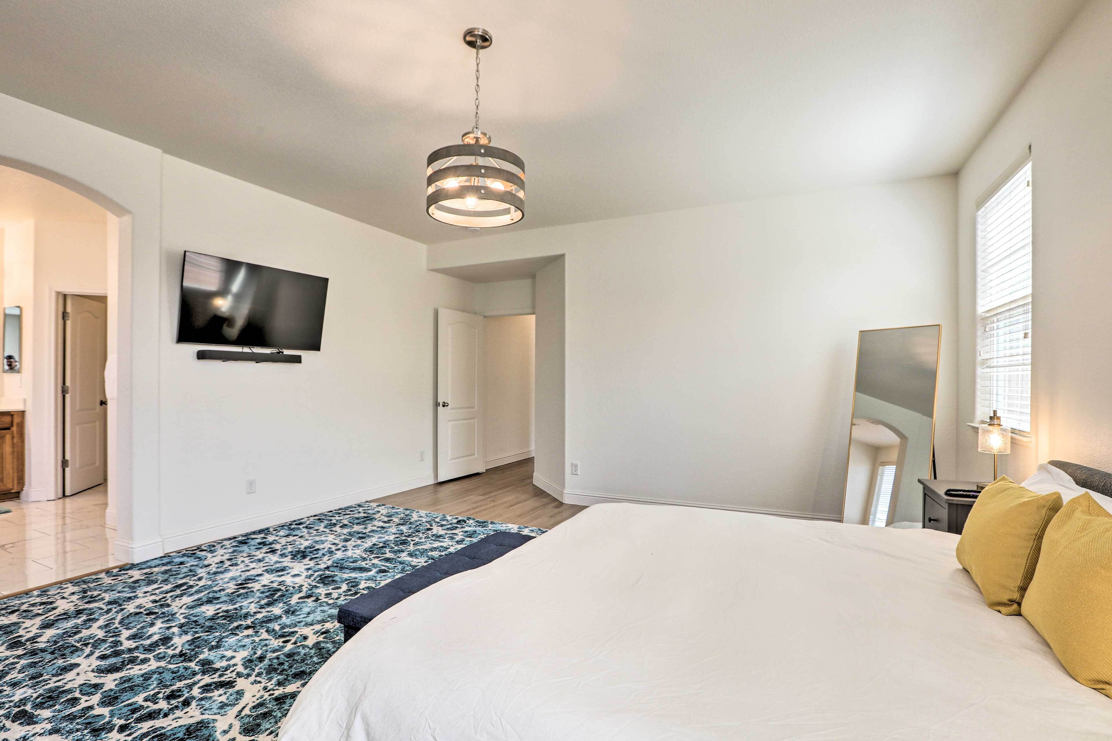 Een moderne slaapkamer met een groot bed, een flatscreen televisie aan de muur, een plafondlamp en een raam met jaloezieën.