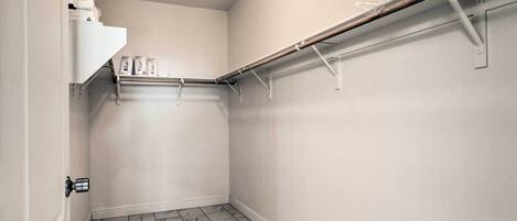 A small, white-walled closet with a wooden rod and shelves, marble-patterned floor, and a door with a modern handle.