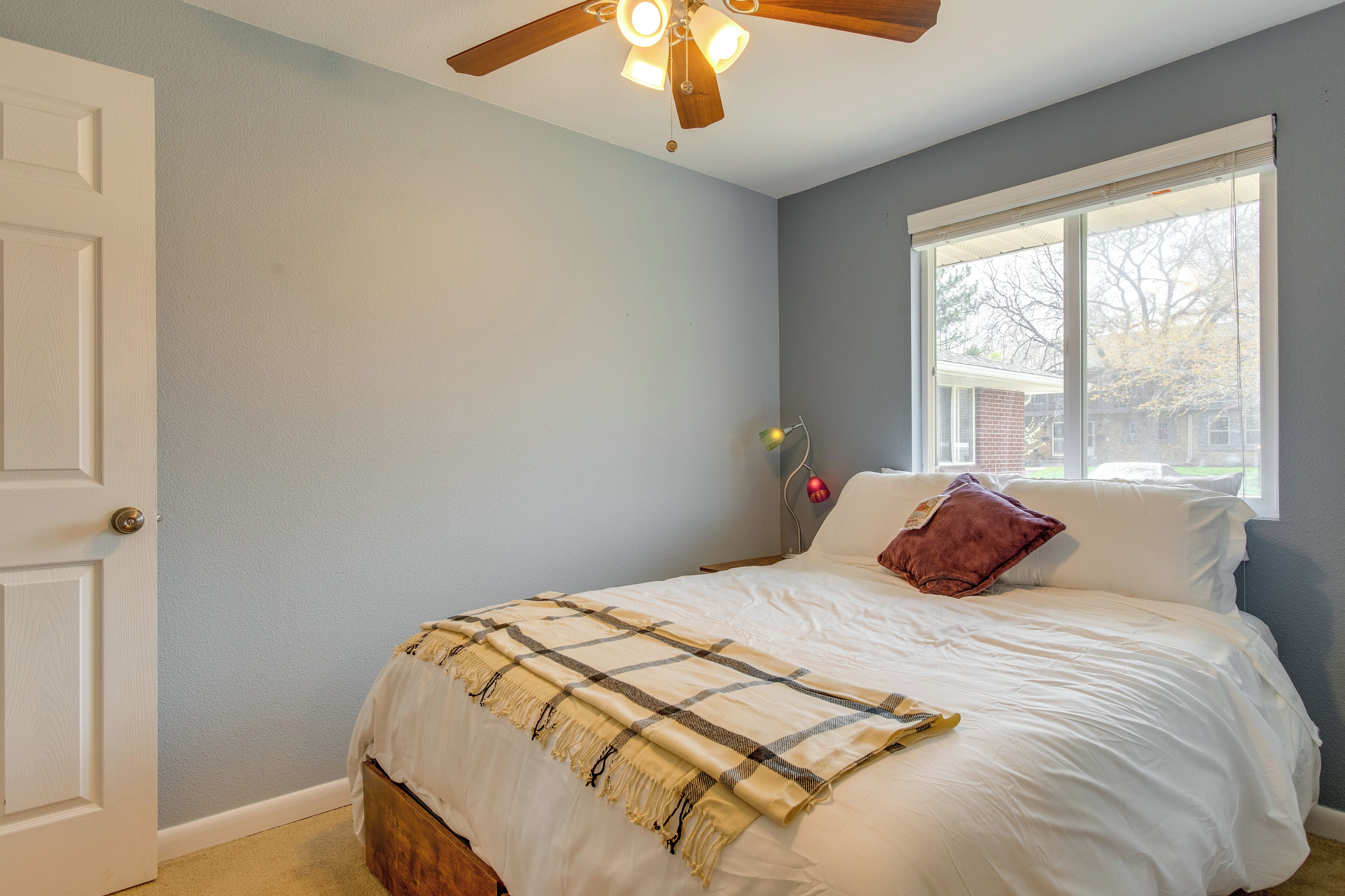 A bedroom with a bed, a ceiling fan, a window with blinds, and a door.