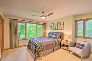 A bedroom with a large bed, a chair, a nightstand, a ceiling fan, and windows with curtains. - Quiet Riverfront Escape With Deck & Fly Fishing! (Sapphire)