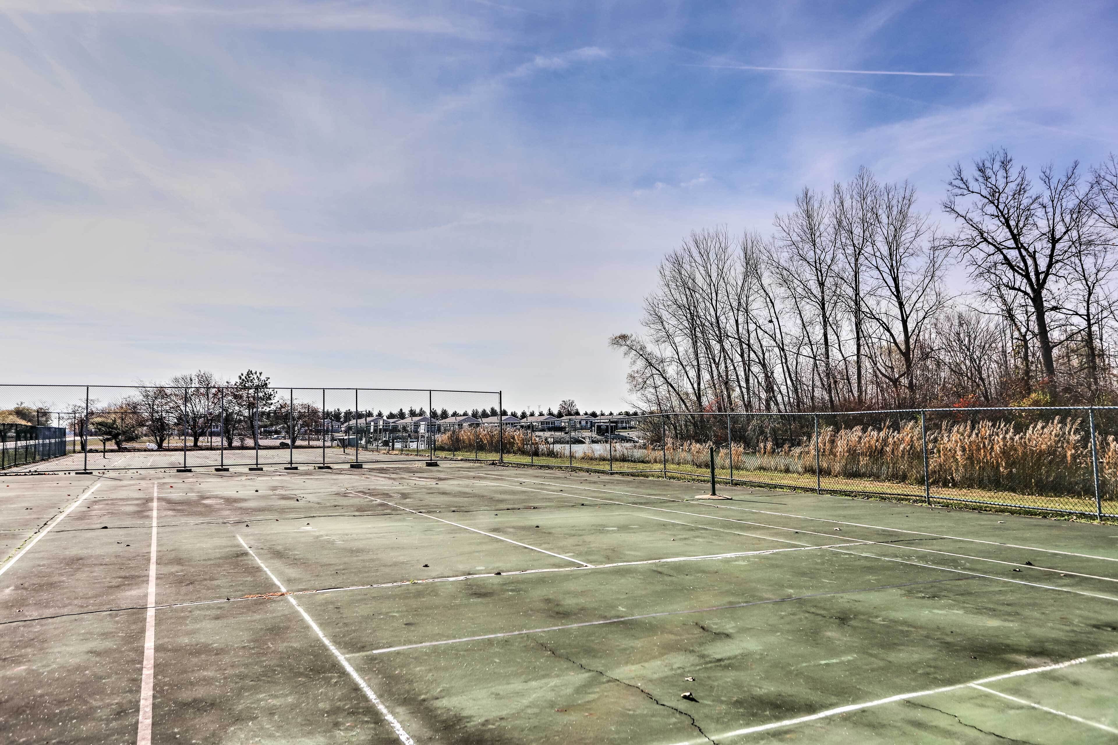An outdoor tennis court with a clear sky and leafless trees in the background.