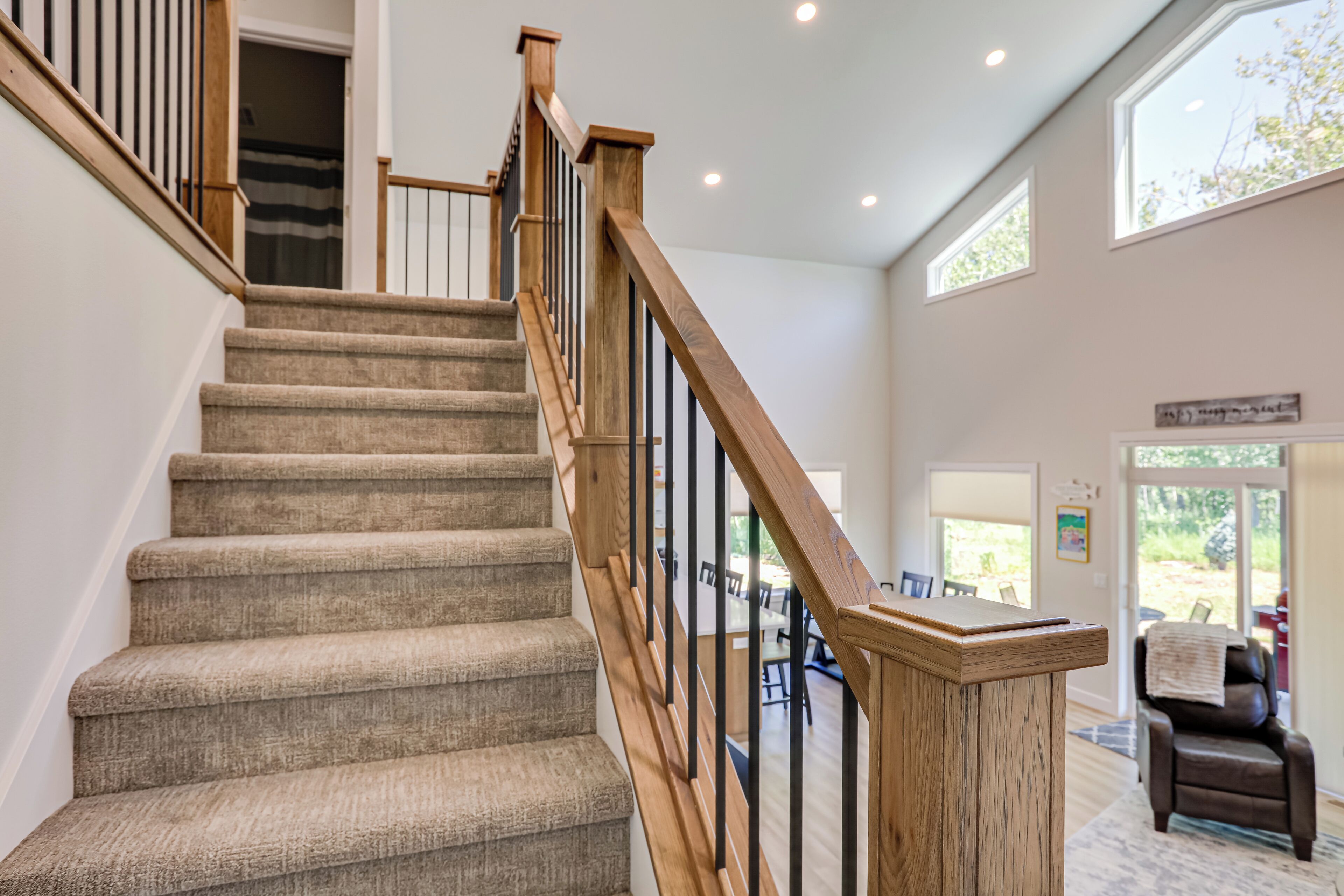 A staircase with wooden railings and carpeted steps leading to a room with a dining area and a view of the outdoors.