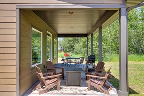 Un patio couvert avec une table et des chaises, un barbecue et une vue sur une zone herbeuse.