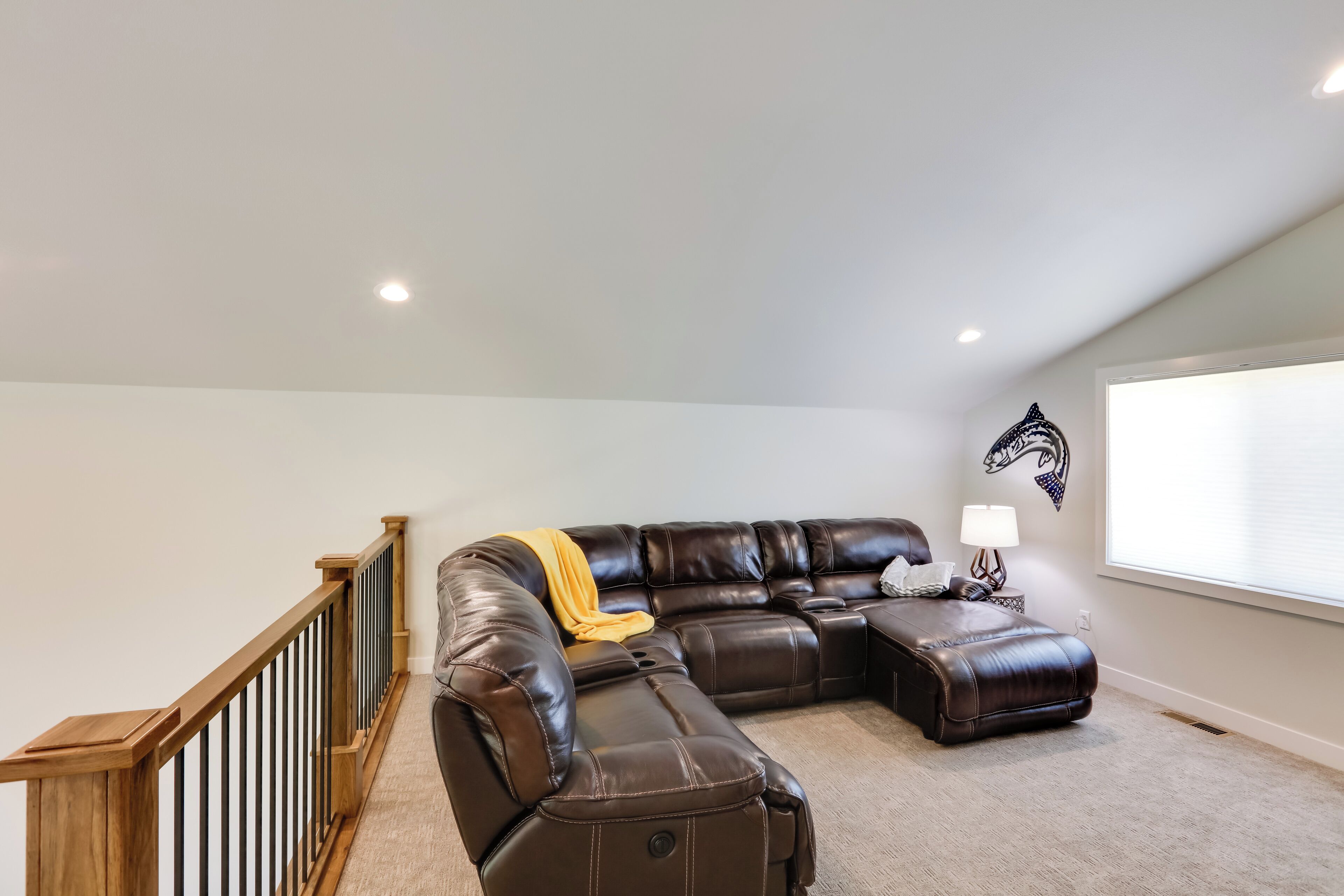 A spacious living room with a sectional sofa, a wooden staircase, and a wall-mounted fish decal.
