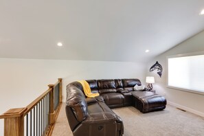 A spacious living room with a sectional sofa, a wooden staircase, and a wall-mounted fish decal. - Creek Access + Fire Pit! Red Lodge Family Retreat (Red Lodge)