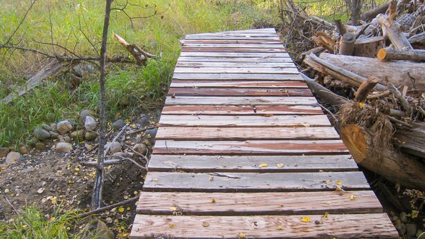Ein Holzweg durch eine natürliche Umgebung mit Felsen und Vegetation zu beiden Seiten.