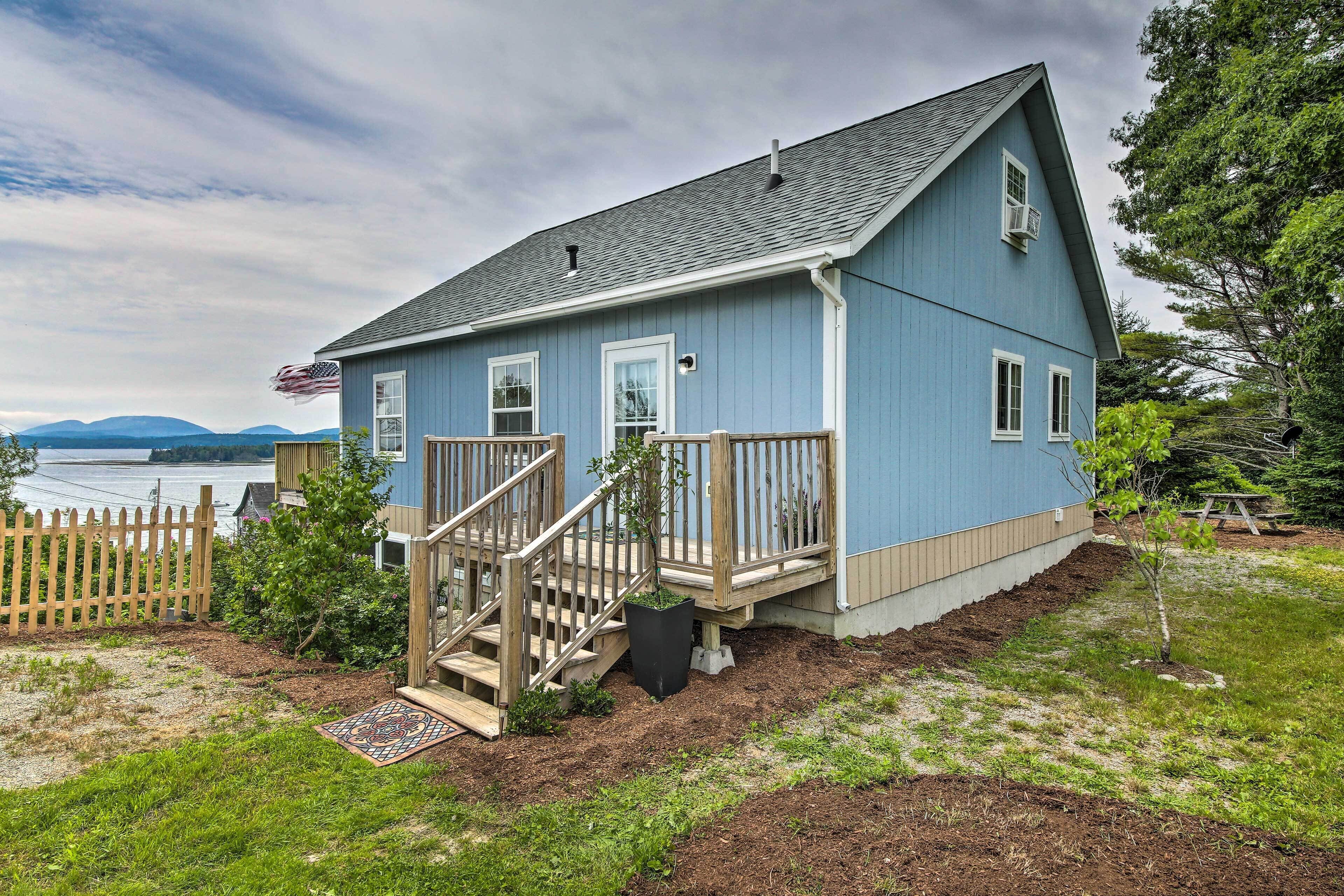 A blue house with a wooden deck and a small staircase leading to the front door.