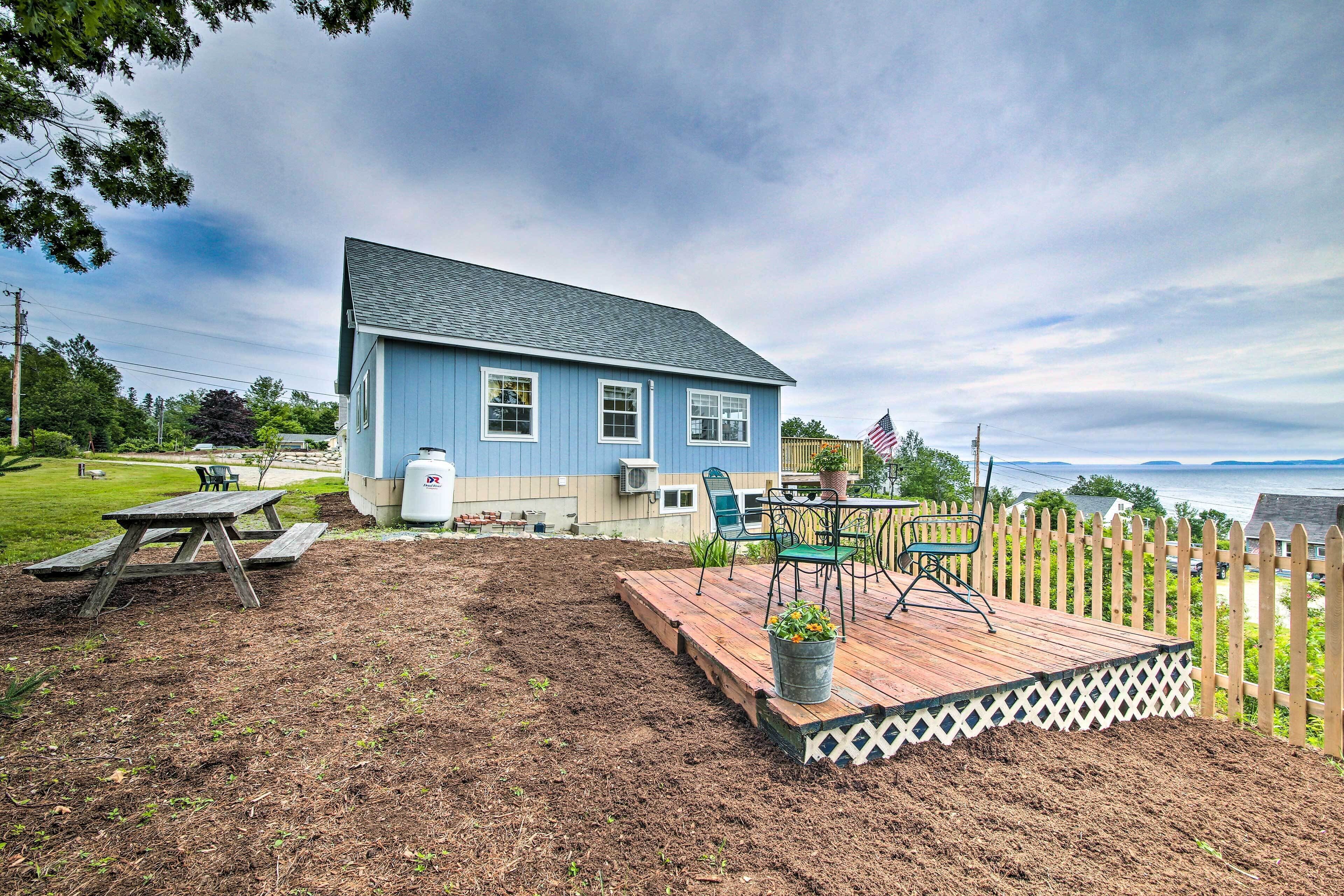 A blue house with a deck, a picnic table, and a view of the ocean.