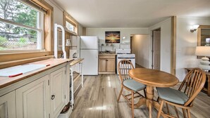 A compact kitchen with a dining area, wooden cabinets, a white refrigerator, and a window overlooking the outdoors. - Acadia Home With Incredible Frenchman Bay View! (Ellsworth)