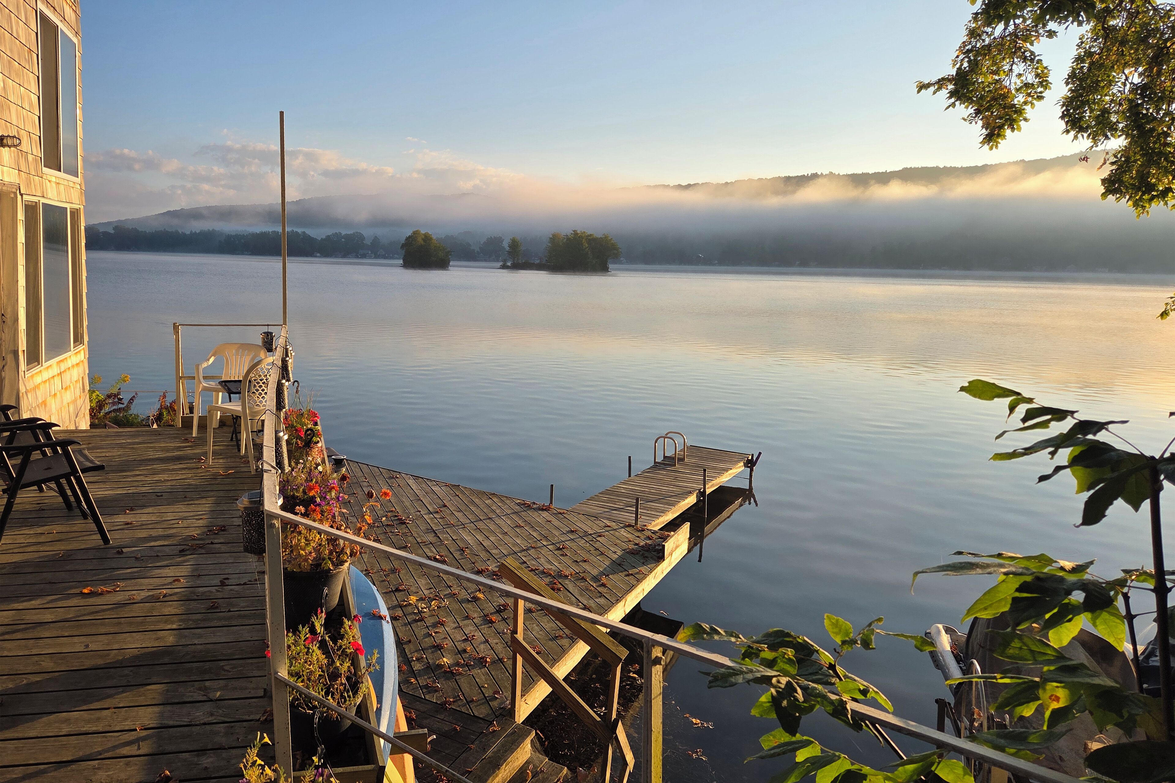 A wooden dock extending over calm water, with a chair and a potted plant on the deck.