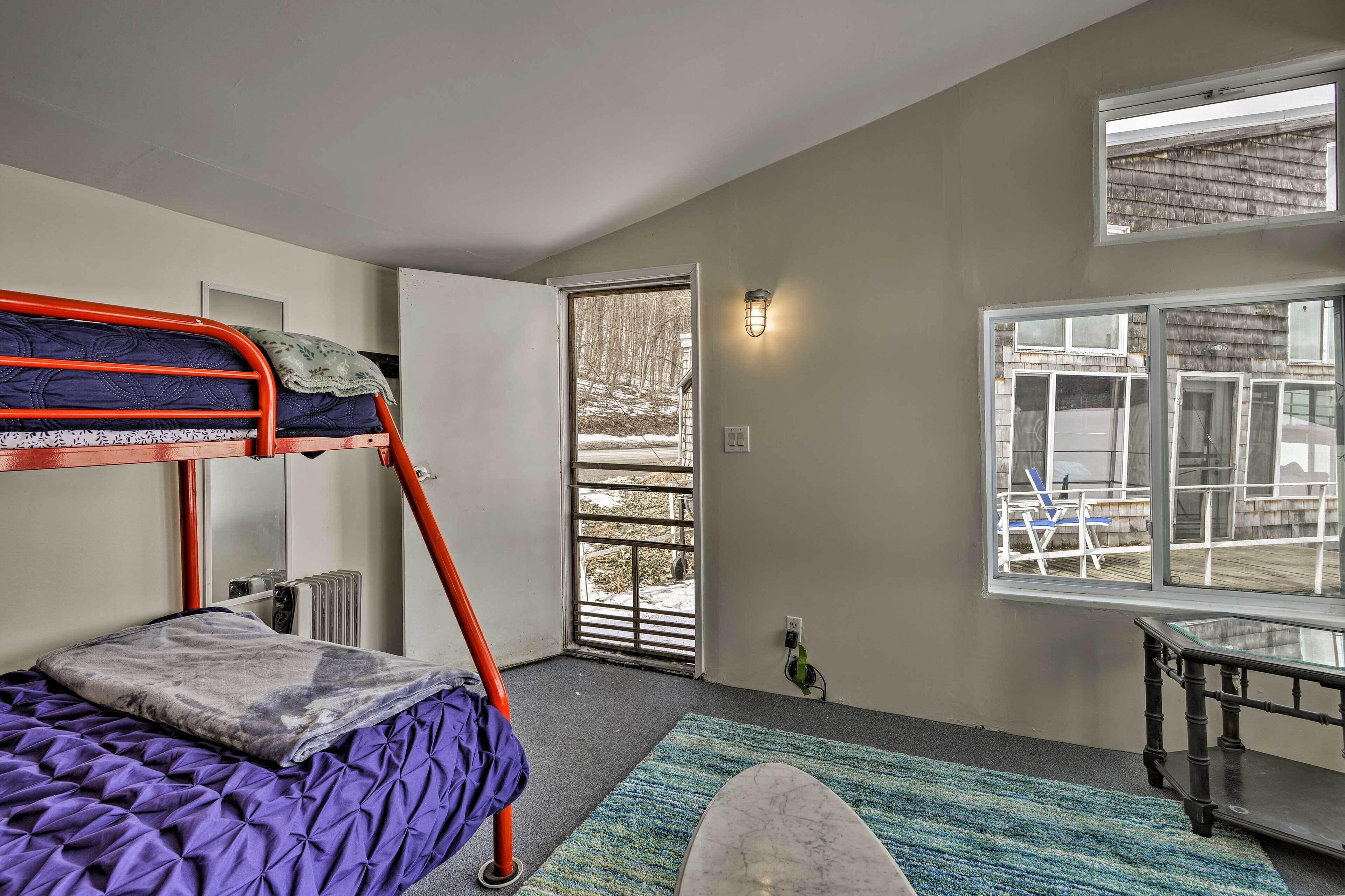 A room with a bunk bed, a small table, a window with a view of the outside, and a door leading to a balcony.