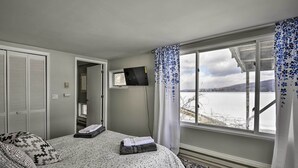 Ein Schlafzimmer mit einem Bett, einem Fernseher an der Wand und einem Fenster mit Vorhängen.