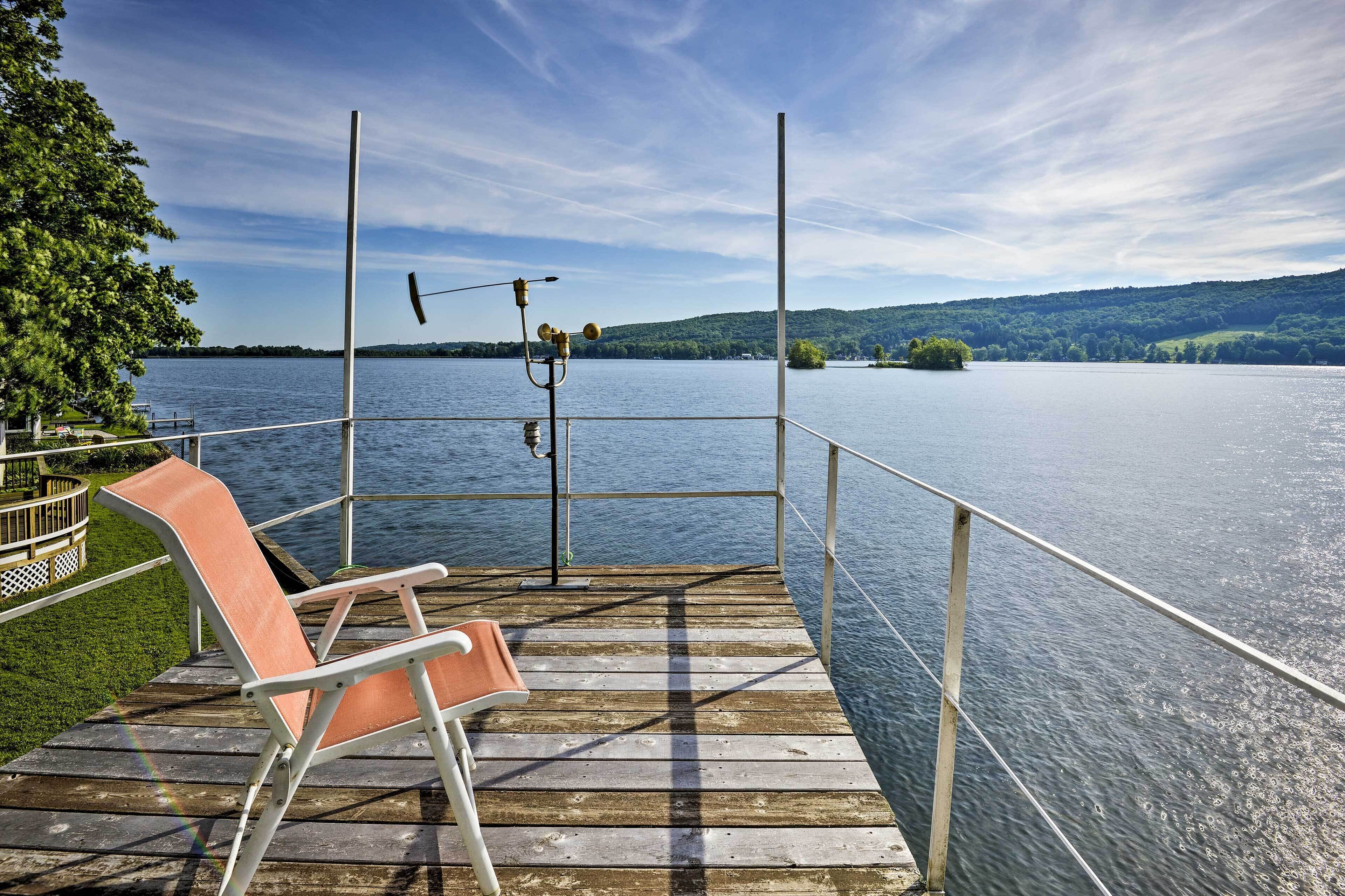 Une terrasse en bois avec une chaise, une rambarde et une vue sur un lac paisible, avec des collines qui se dessinent à l’horizon.