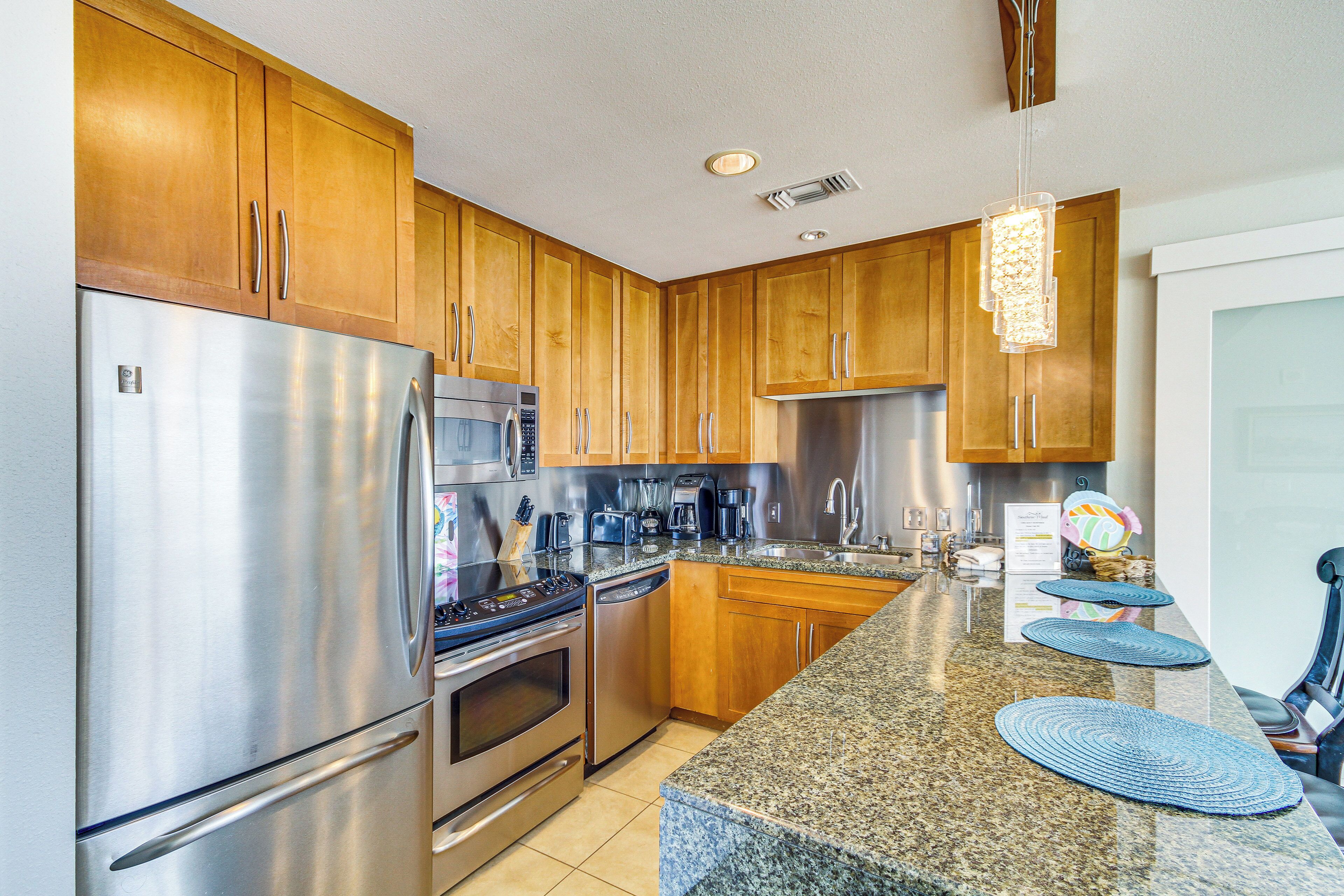 Eine moderne Küche mit Holzschränken, Edelstahlgeräten, Granitarbeitsplatten und einer Pendelleuchte.