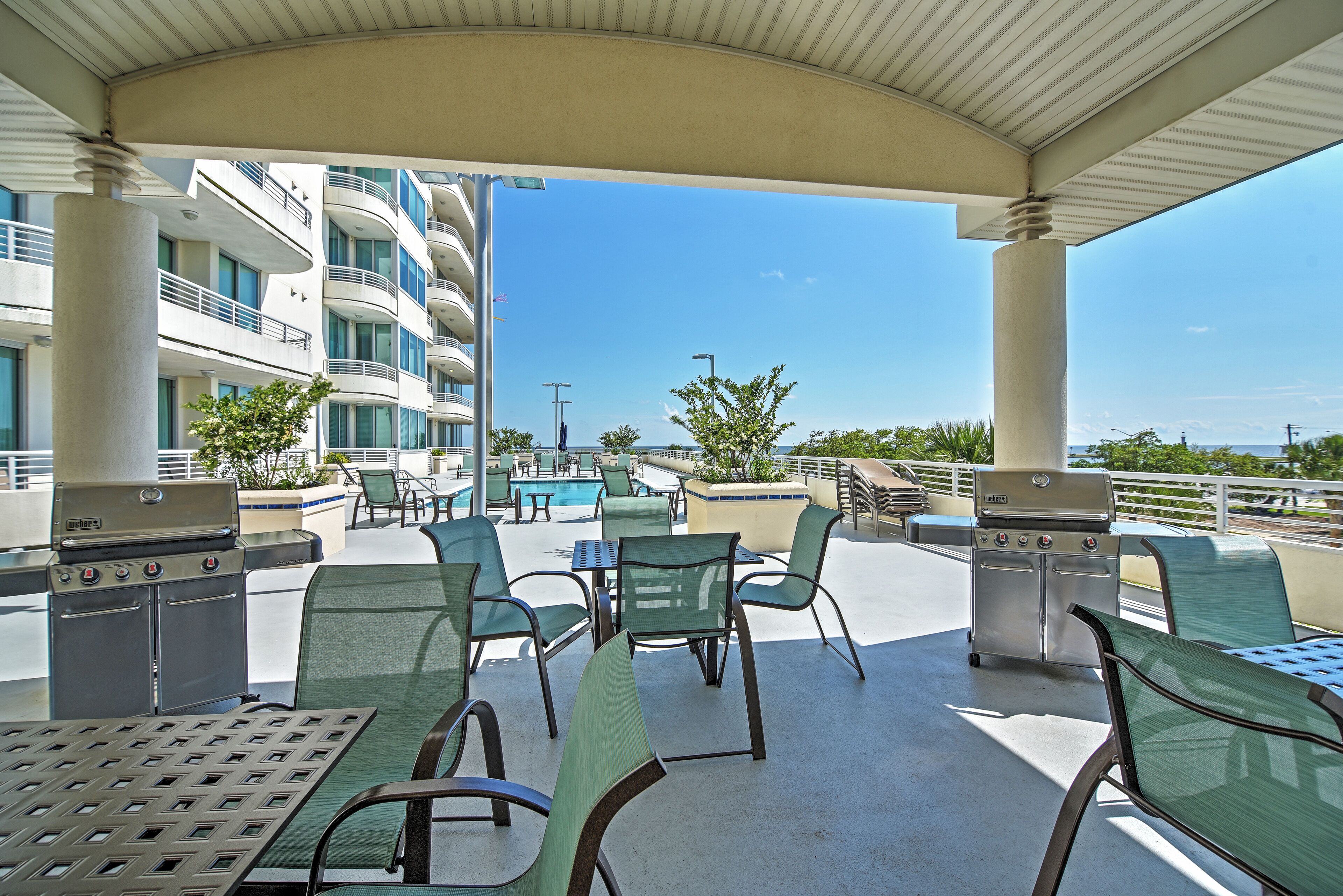 An outdoor patio with seating and barbecue grills, overlooking a pool and a building with balconies.