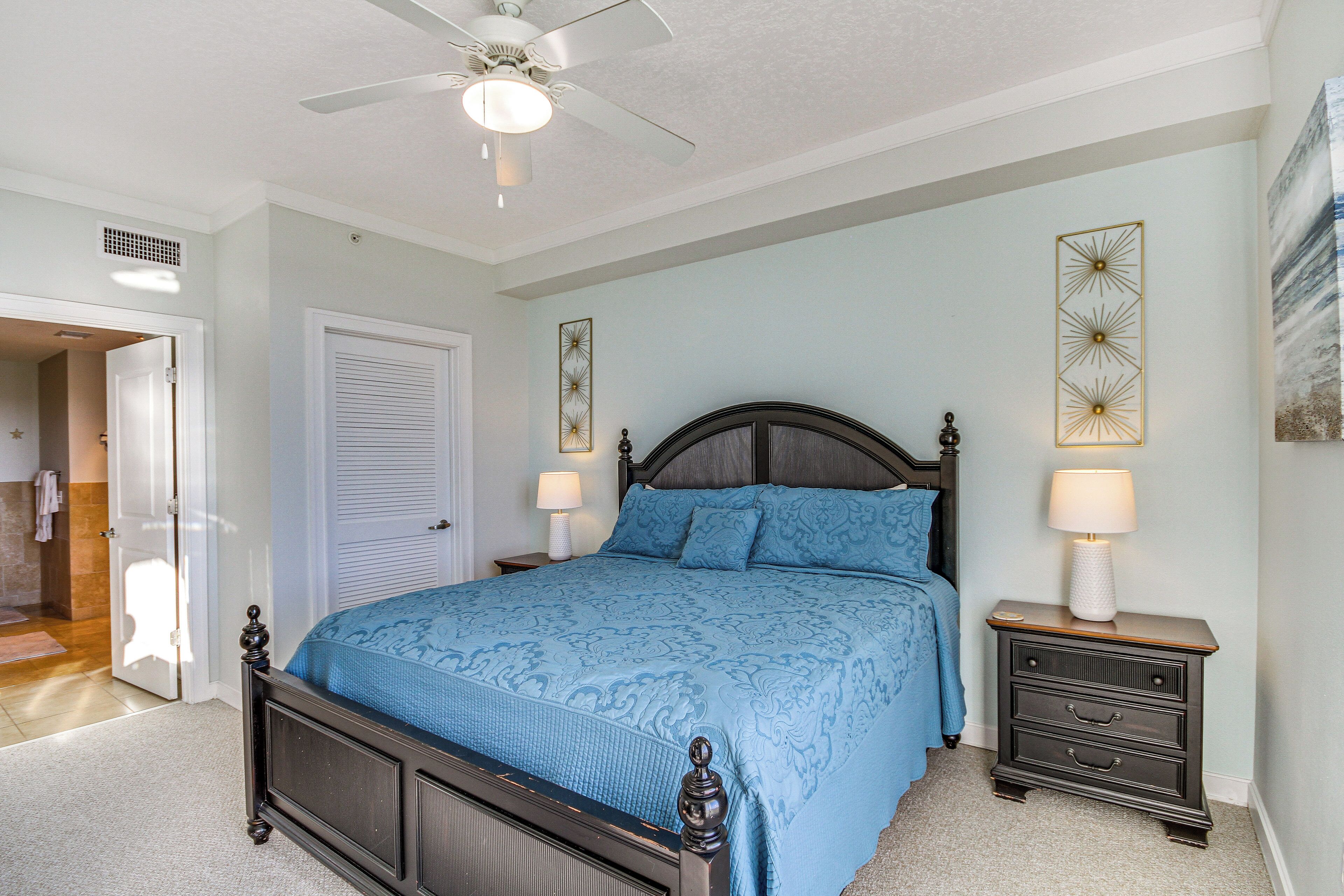 A bedroom with a large bed, a nightstand with a lamp, and a ceiling fan.