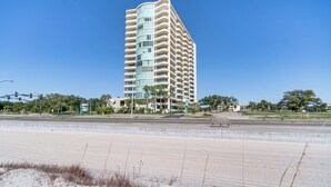 A tall, multi-story hotel with a curved facade, located near a beach with sand dunes and sparse vegetation. - Beachside Biloxi Club Condo: Balcony w/ Ocean View (Biloxi)