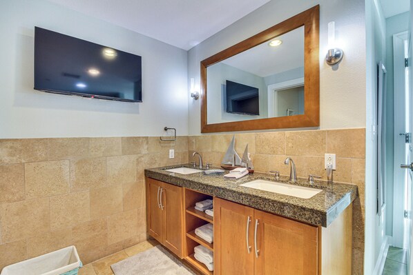 Une salle de bain avec deux lavabos, un grand miroir et un téléviseur à écran plat fixé au-dessus des lavabos.
