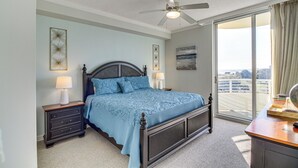 A bedroom with a large bed, a nightstand, a dresser, a ceiling fan, and a view of the outdoors through a sliding glass door. - Beachside Biloxi Club Condo: Balcony w/ Ocean View (Biloxi)