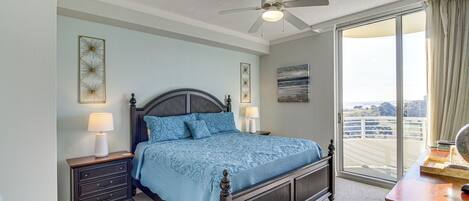 A bedroom with a large bed, a nightstand, a dresser, a ceiling fan, and a view of the outdoors through a sliding glass door.